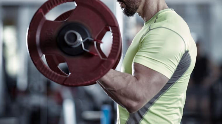 Muscular person in gym doing barbell curl